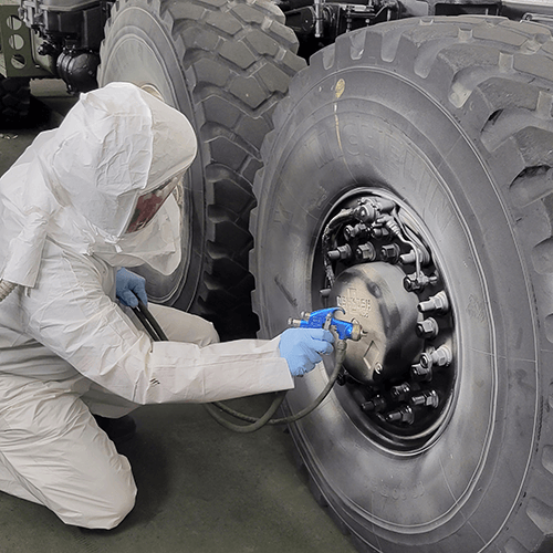 A paint technician in protective painting uniform paints the hub of one tire