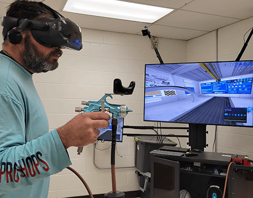 a man wearing a virtual reality googles and vr paint gun stands before a screen showing a scene from the VirtualPaint training program