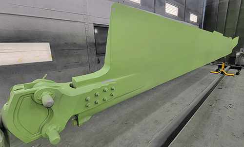 a long blade like piece of military equipment sits inside a paint spray booth post painting