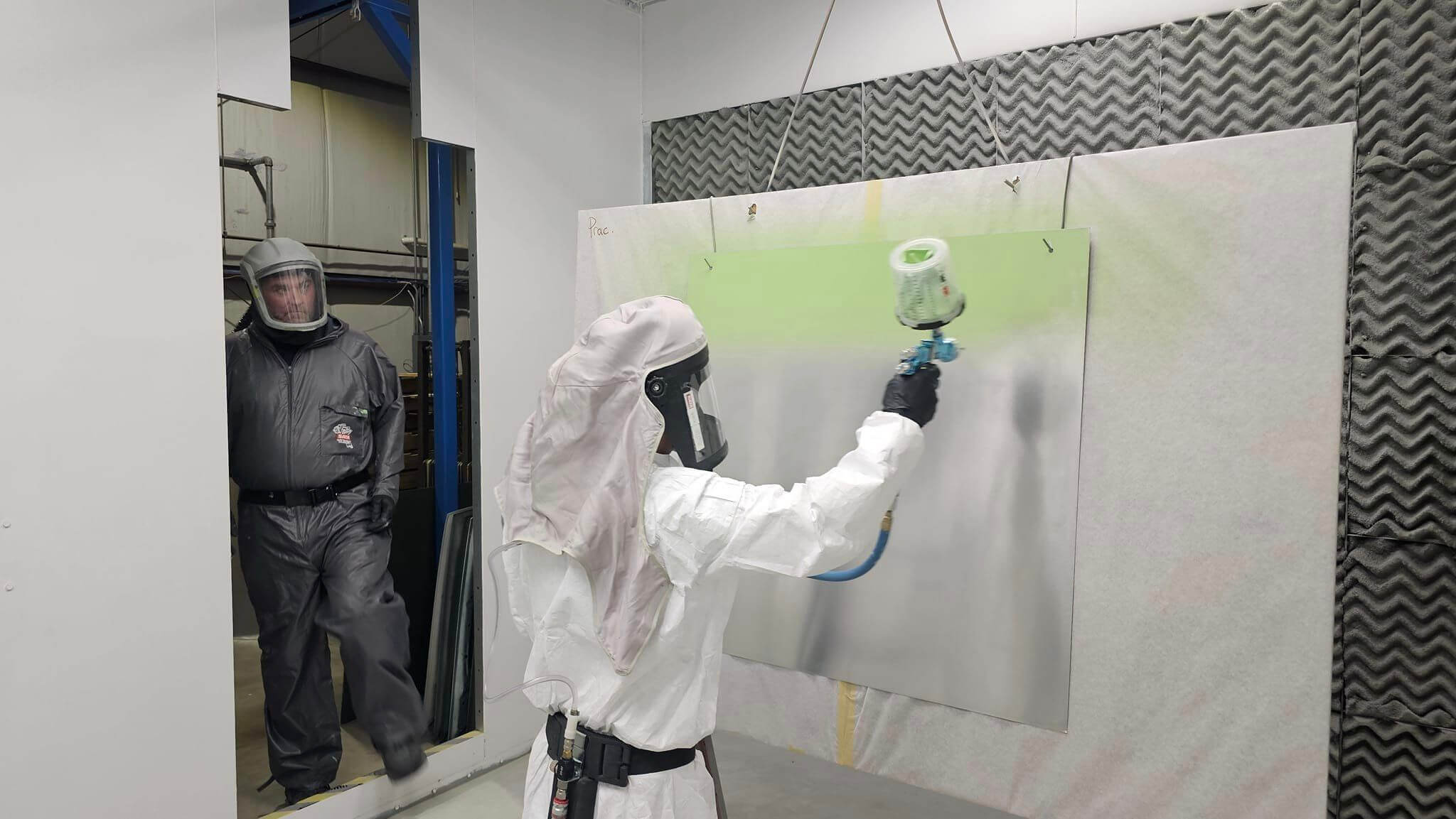 man in paint booth wearing protective gear while trainer observes