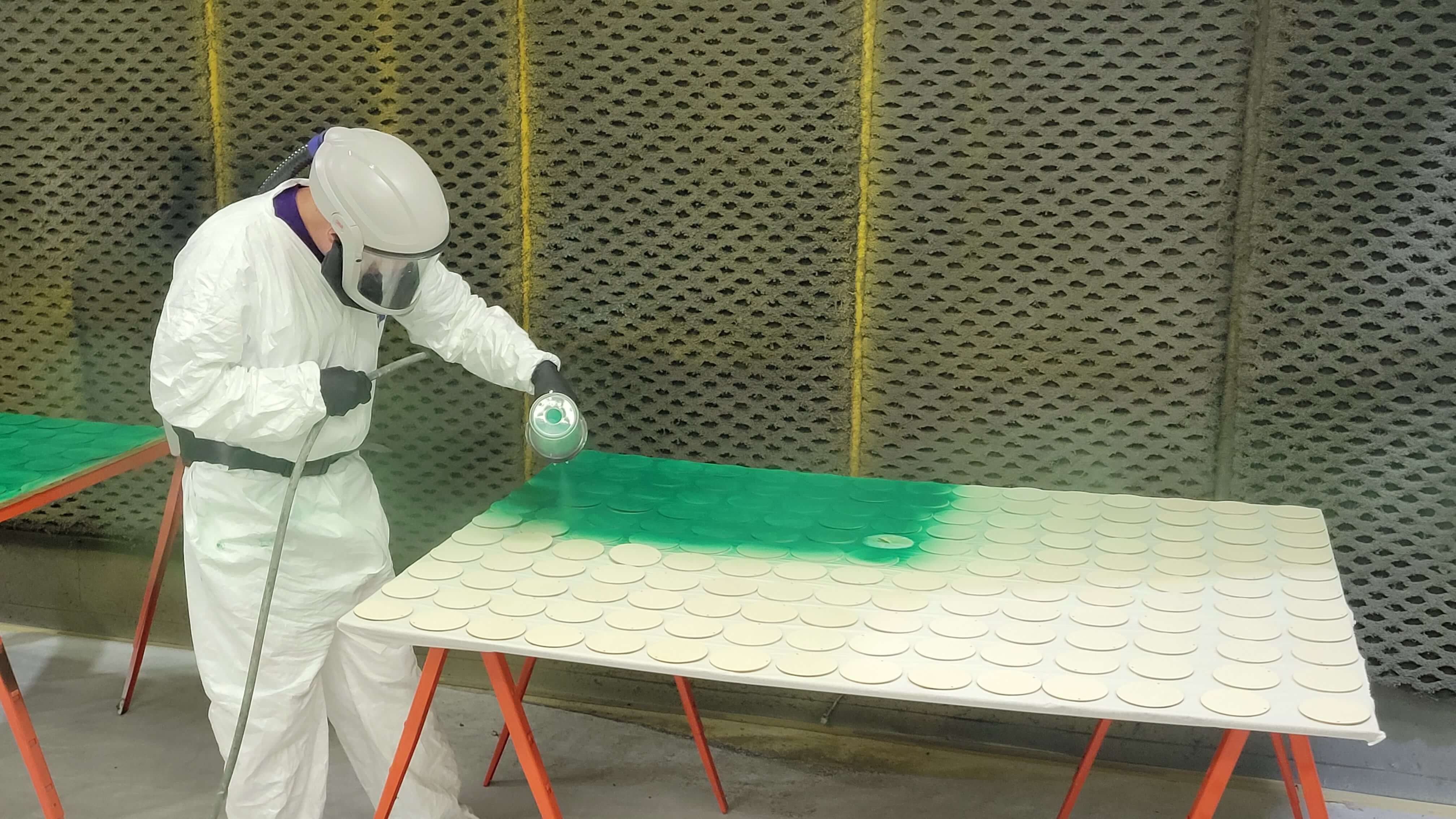 An IWRC Painting Trainee in protective paint suit paints green dots for UNI Green Dot Program
