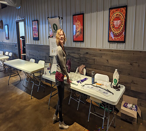 woman smiling as she waits to greet attendees at the Iowa Brewers Conference