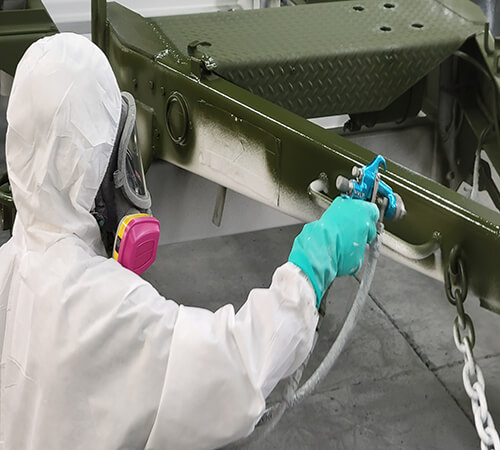 man in white ppe spray painting a military trailer