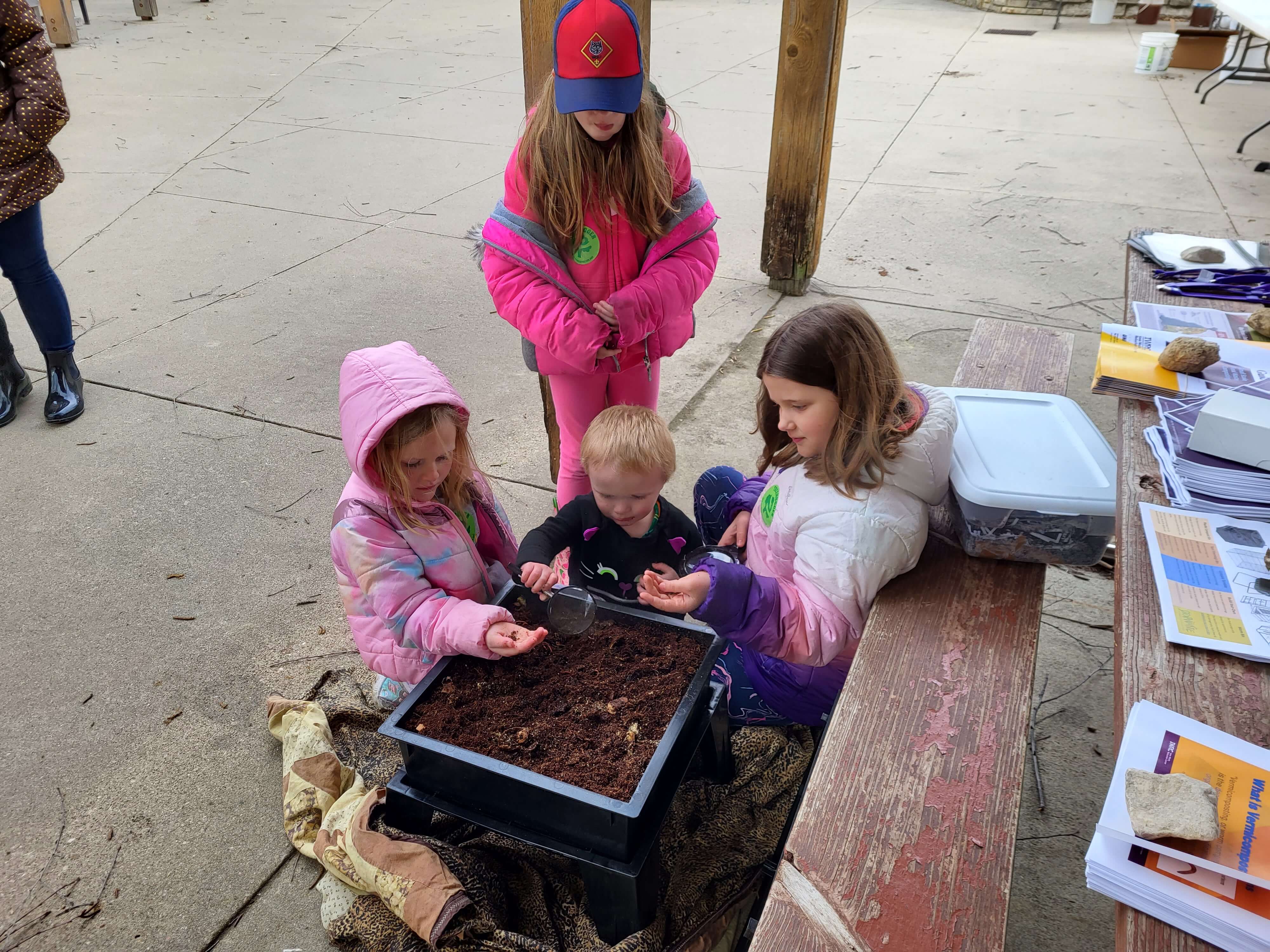 Three children playing with worms in Jason Clays vermicomposting bin at Camp Wakonda's Celebrate Earth Day event