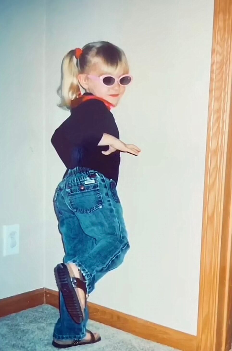 Young Kendall Lienemann, decked out in fashion forward jeans, black shirt, pink rimmed glasses, pigtails and red accents