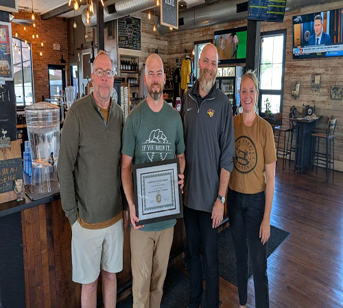 Three men and one woman posing for a picture holding a certificate inside Textile Brewing Company