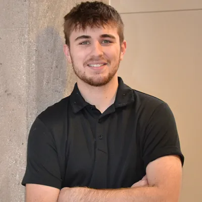 young man in black polo leaning again a cement pilar