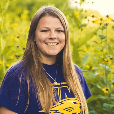 Link, Waste Reduction Coordinator Jordan Henniges standing before field of yellow flowers, profile page