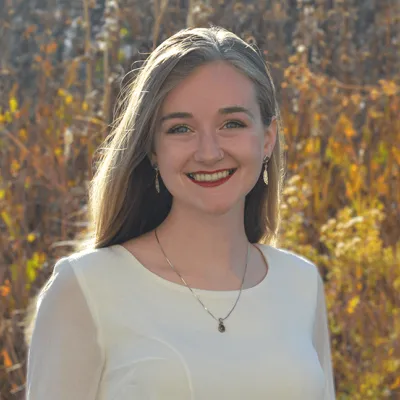 Link, Student intern Paige German stands before field of fall prairie grass, profile page